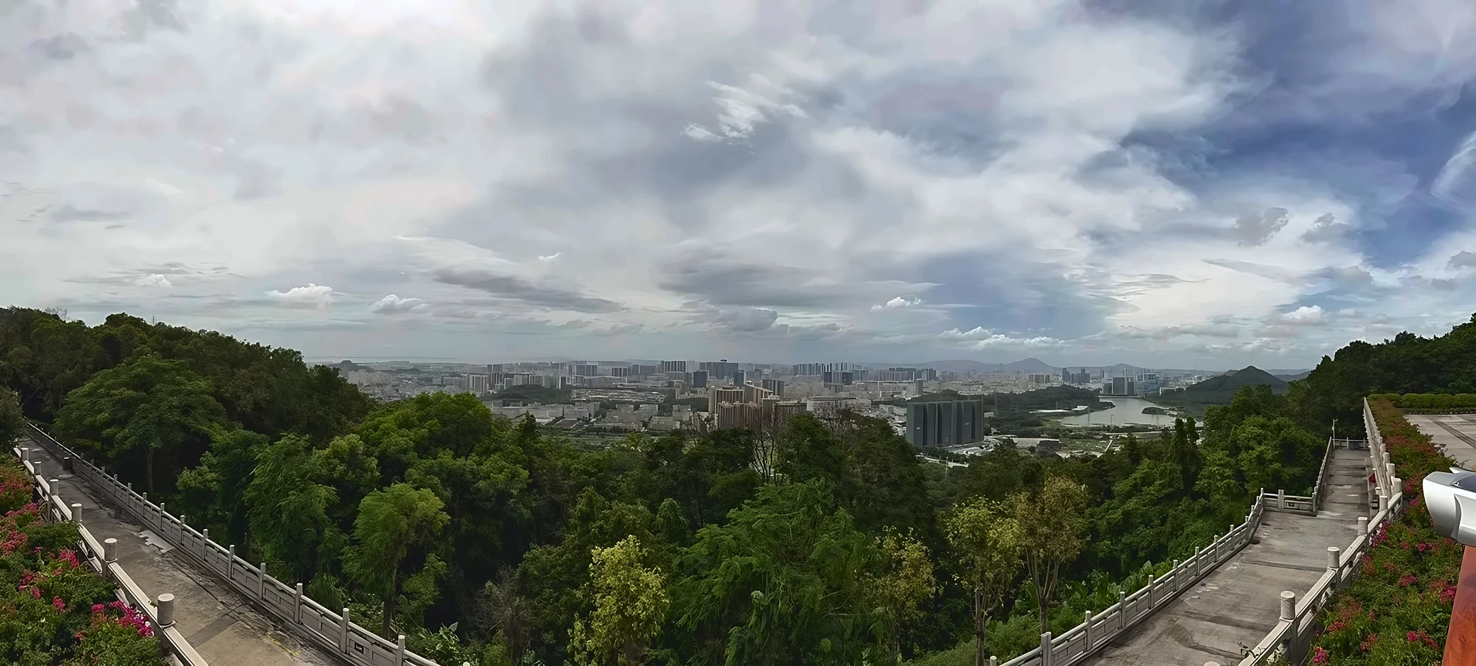 A wide panorama shows stone-railed stairs flanking wooded slopes, with city buildings and a lake in the distance.
