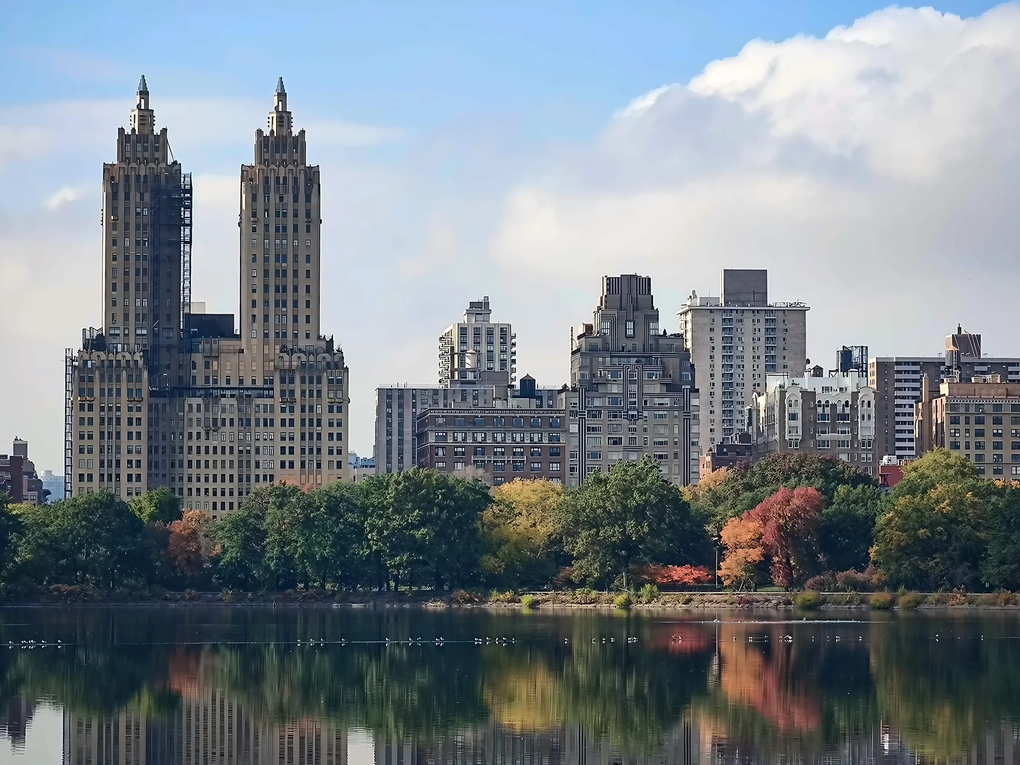 The Eldorado twin towers and neighboring buildings rise above autumn trees and reflections across Central Park's reservoir.