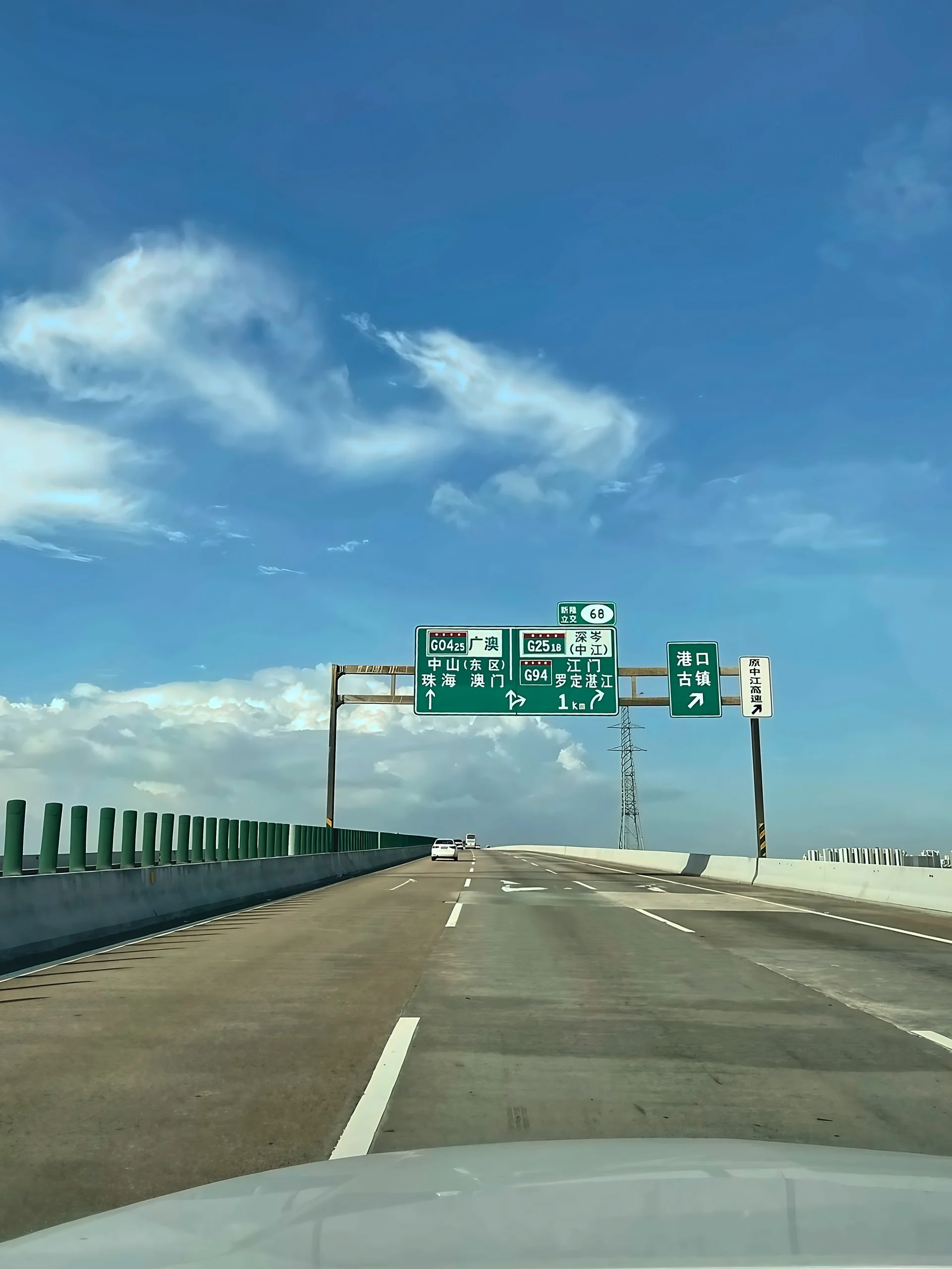 A broad elevated expressway approaches signs for Xinlong Interchange, with a transmission tower beside the road under blue skies.