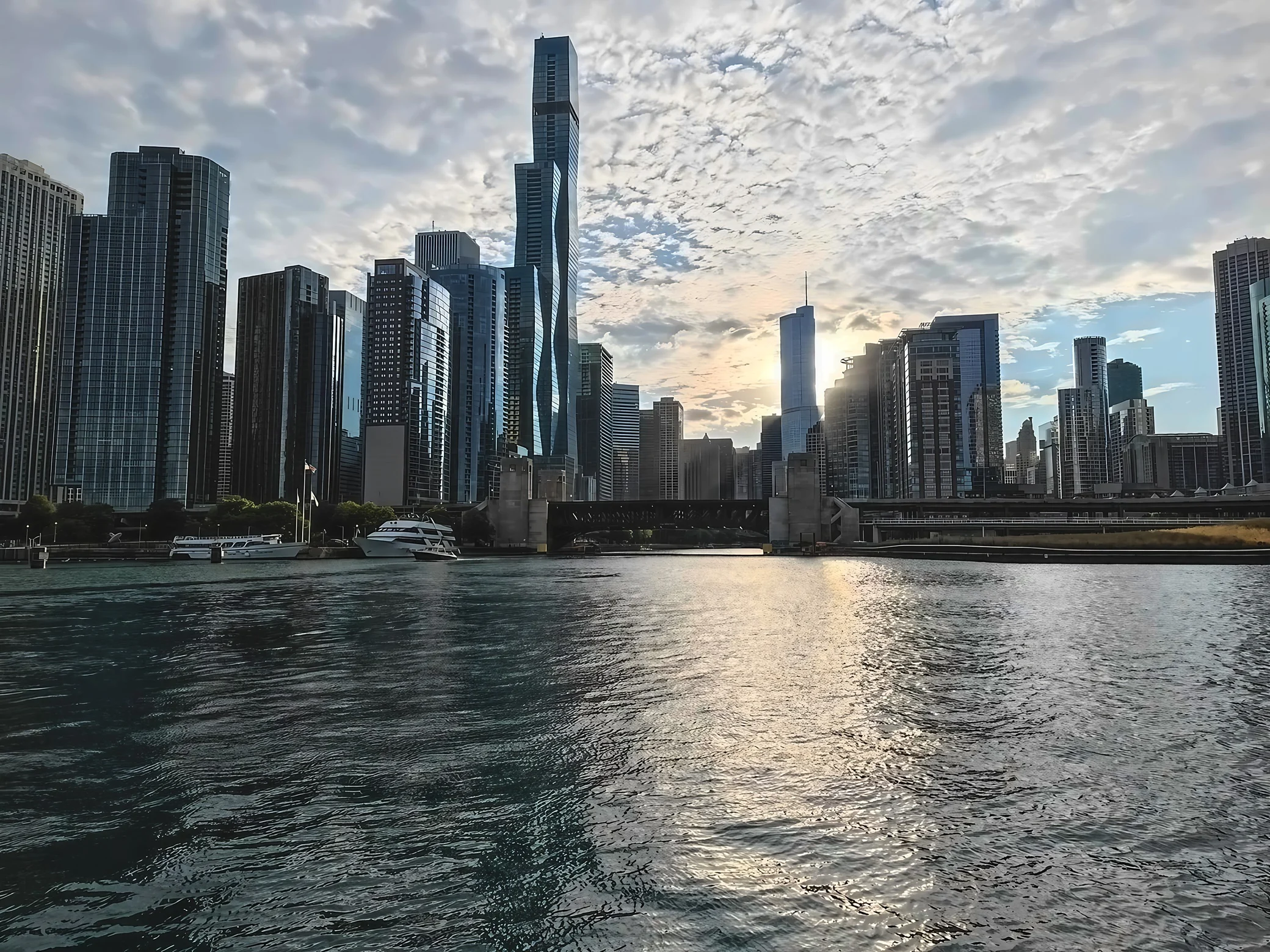 Sunlight shines between Chicago's high-rises and reflects across the rippling river in front of a steel bridge.