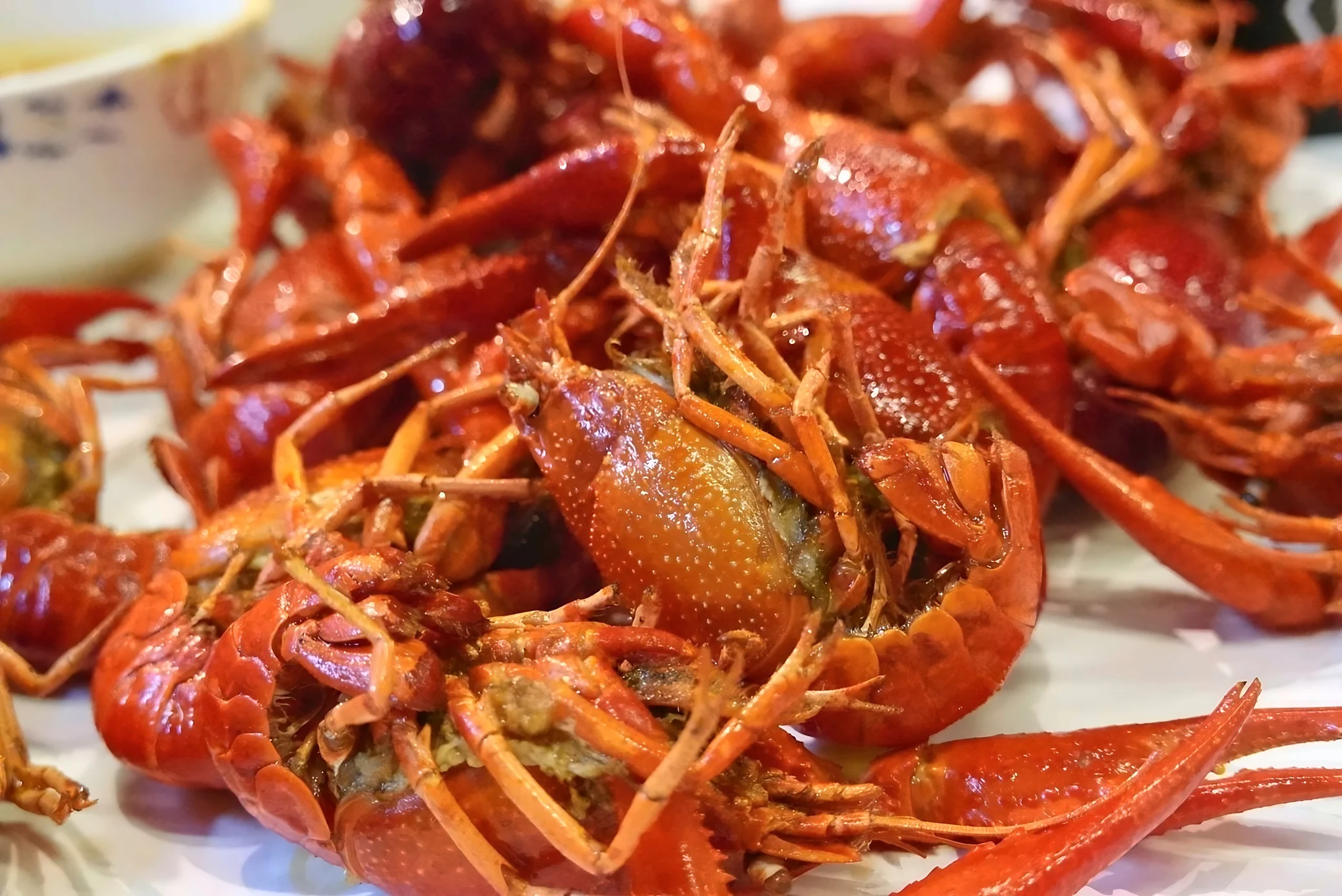 Glossy red cooked crayfish cover a white tabletop in a horizontal close-up emphasizing a central head and large foreground claws.