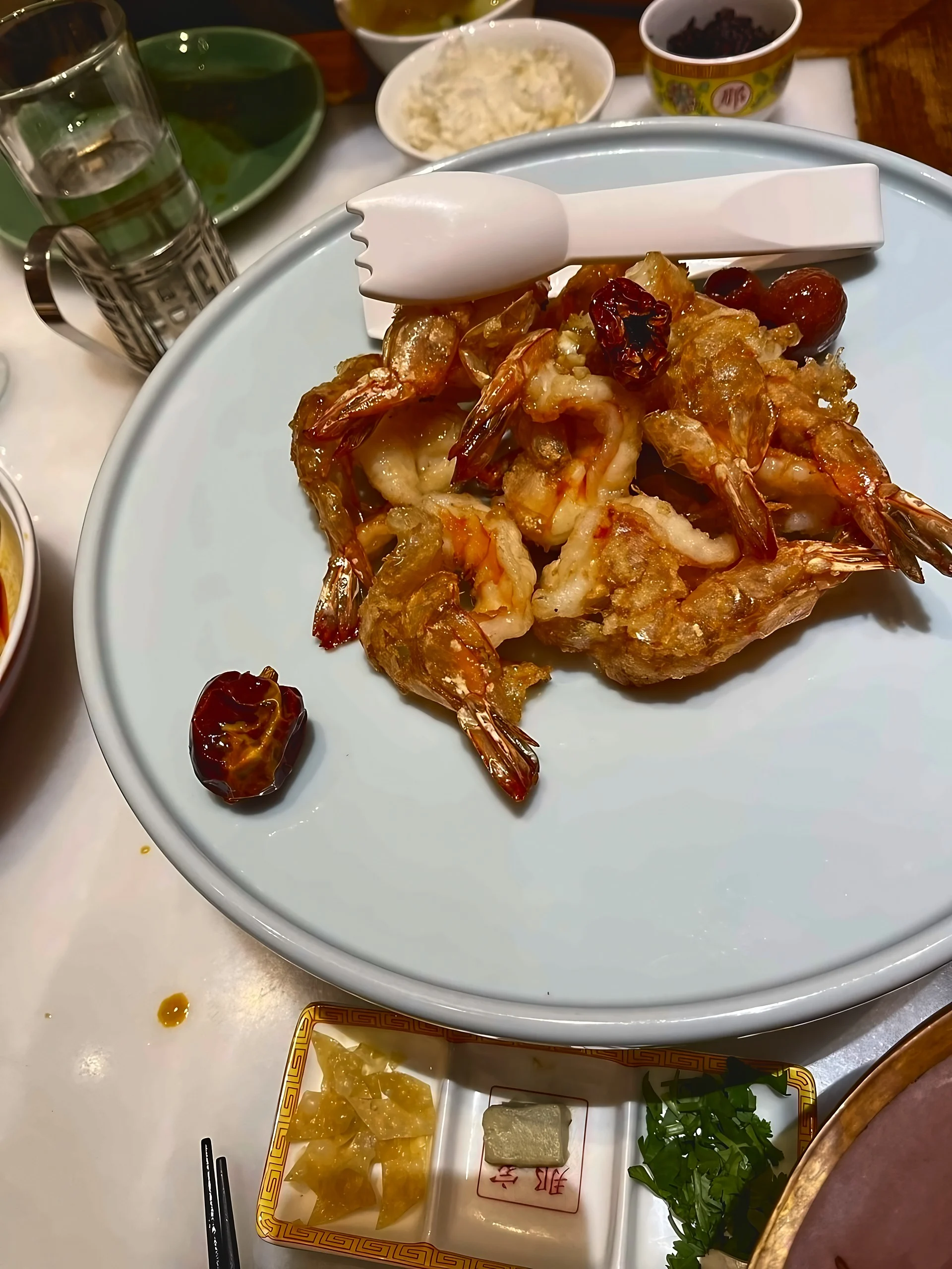 Golden fried shrimp and red dates fill a pale blue platter, with white serving tongs, a condiment tray, rice and a water glass nearby.