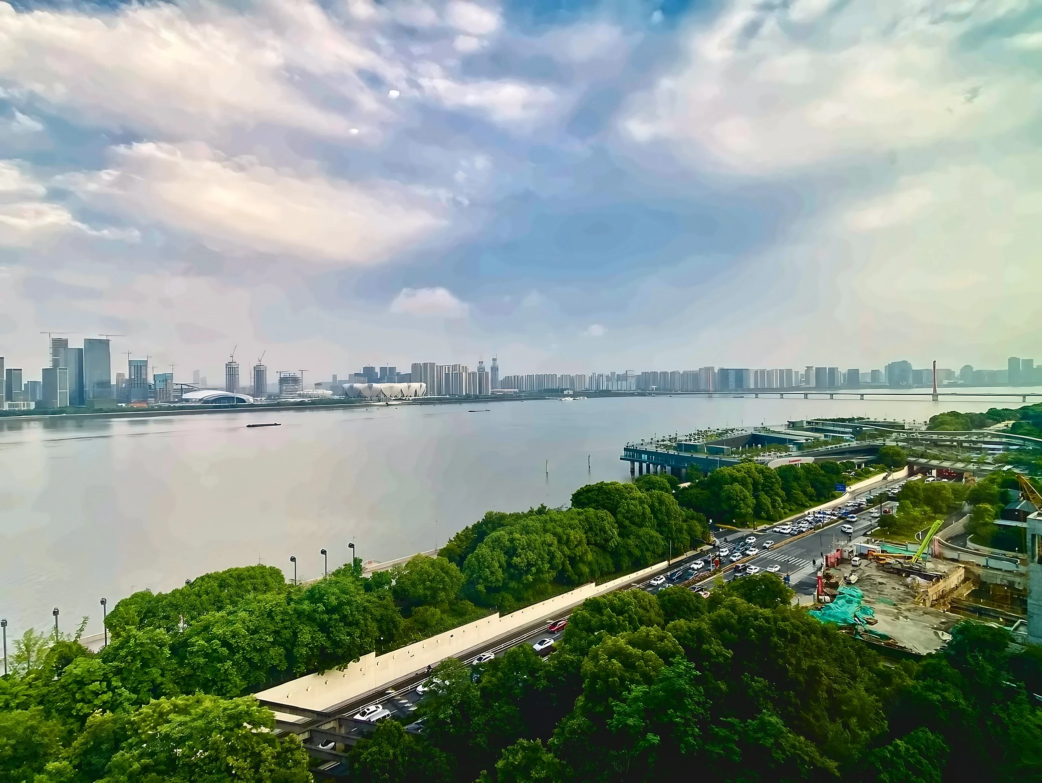 An elevated view spans the Qiantang River, Hangzhou Olympic Sports Center, riverside greenery, traffic and a distant bridge.