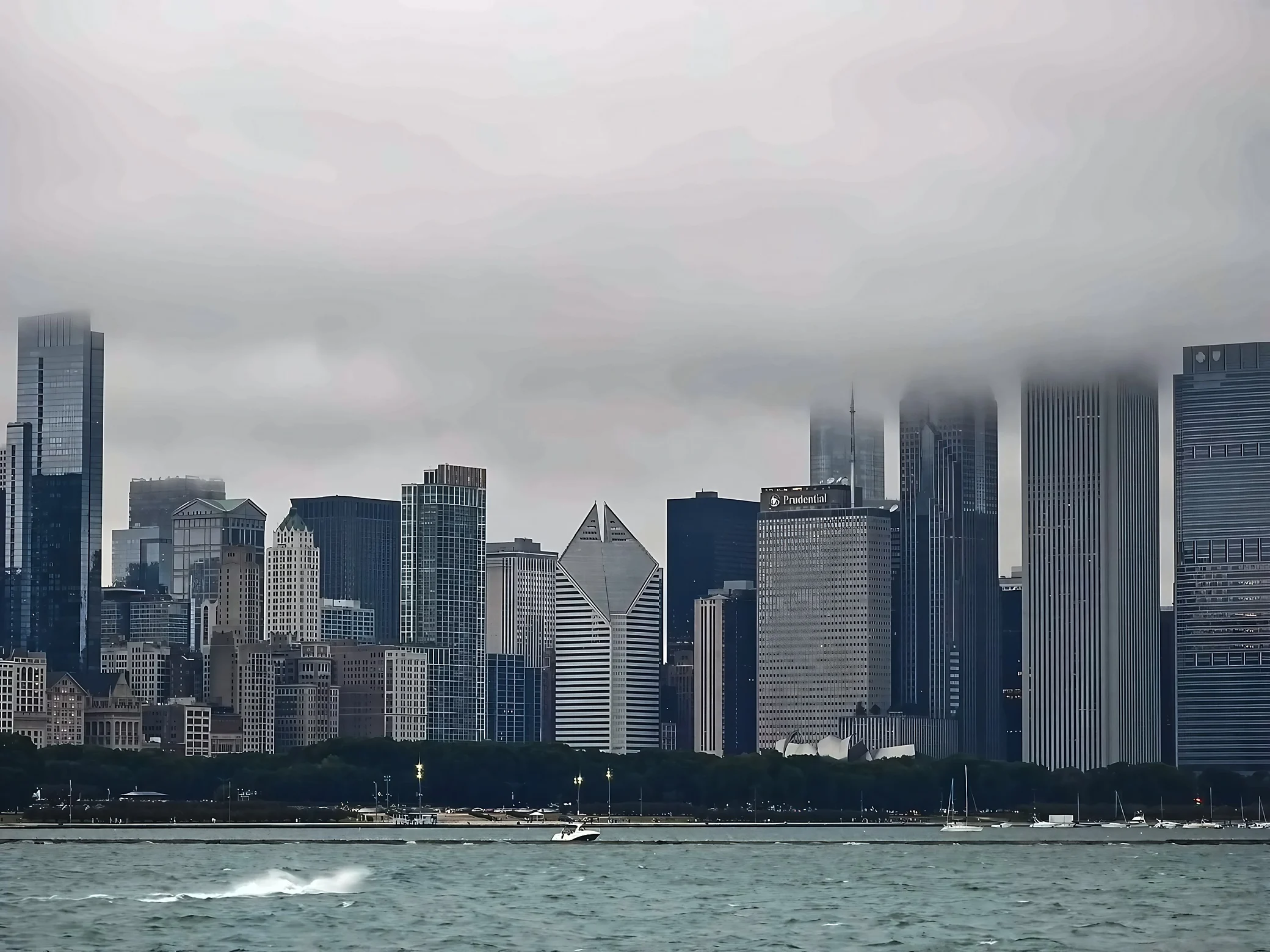 A diamond-roofed tower and the Prudential building stand along Chicago's lakefront beneath cloud-covered skyscrapers, with boats and white spray in the foreground.