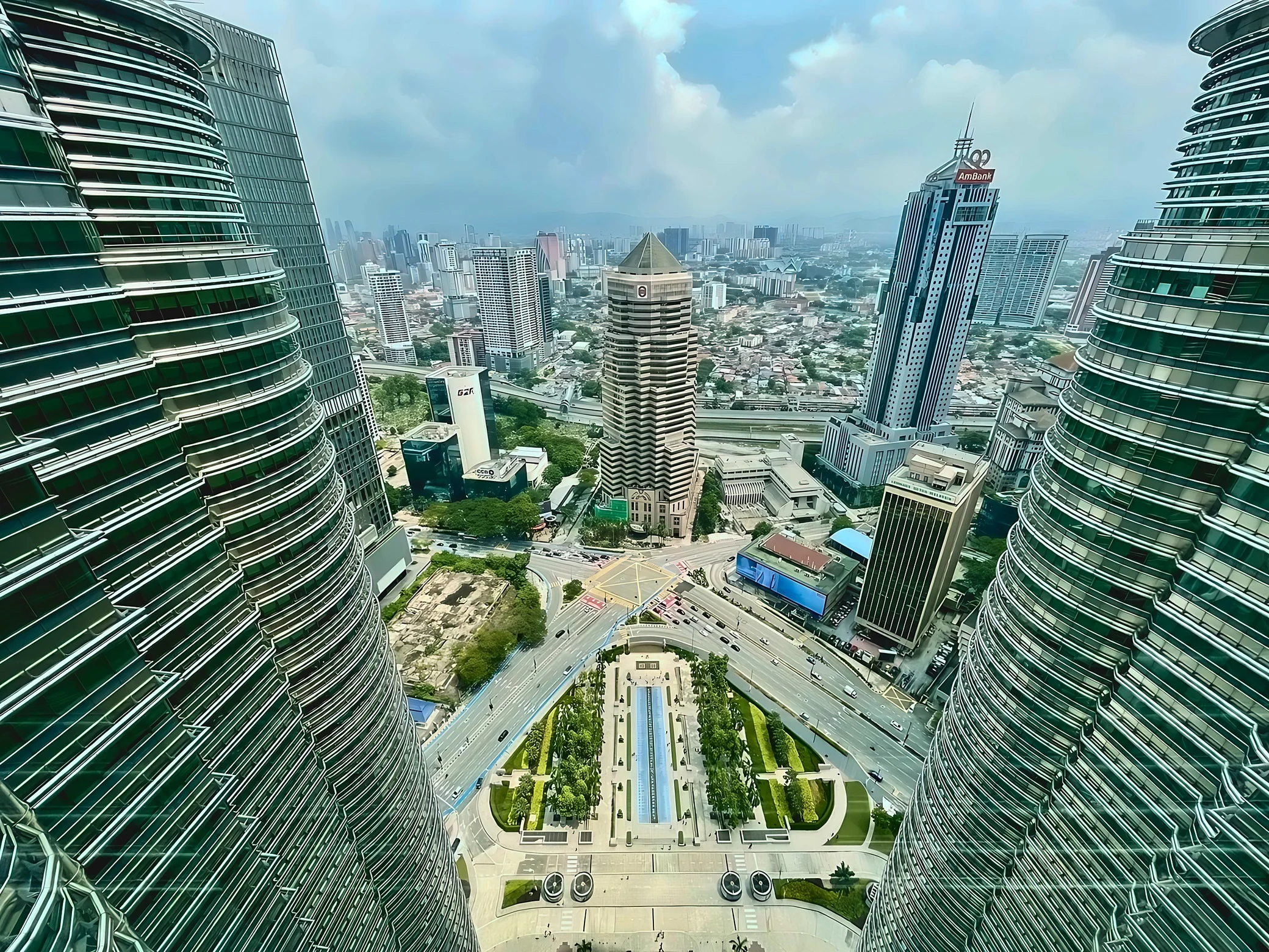 The curved metal facades of the Twin Towers flank a plaza with a long blue pool and a road junction marked by a yellow grid.