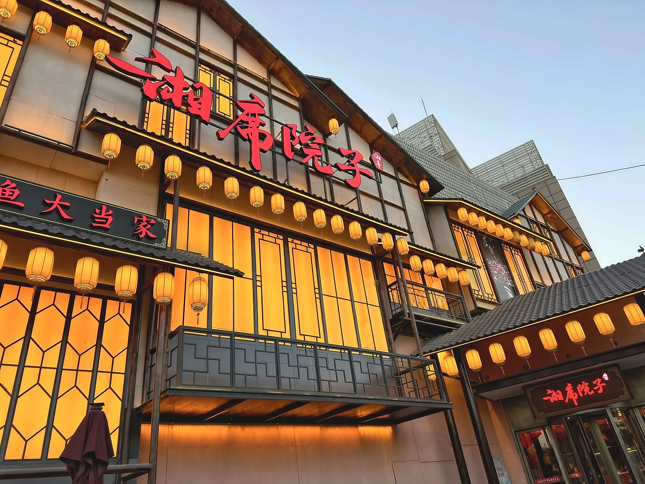 Rows of warm yellow lanterns decorate the traditional-style facade and red signage of a Hunan restaurant in Beijing.