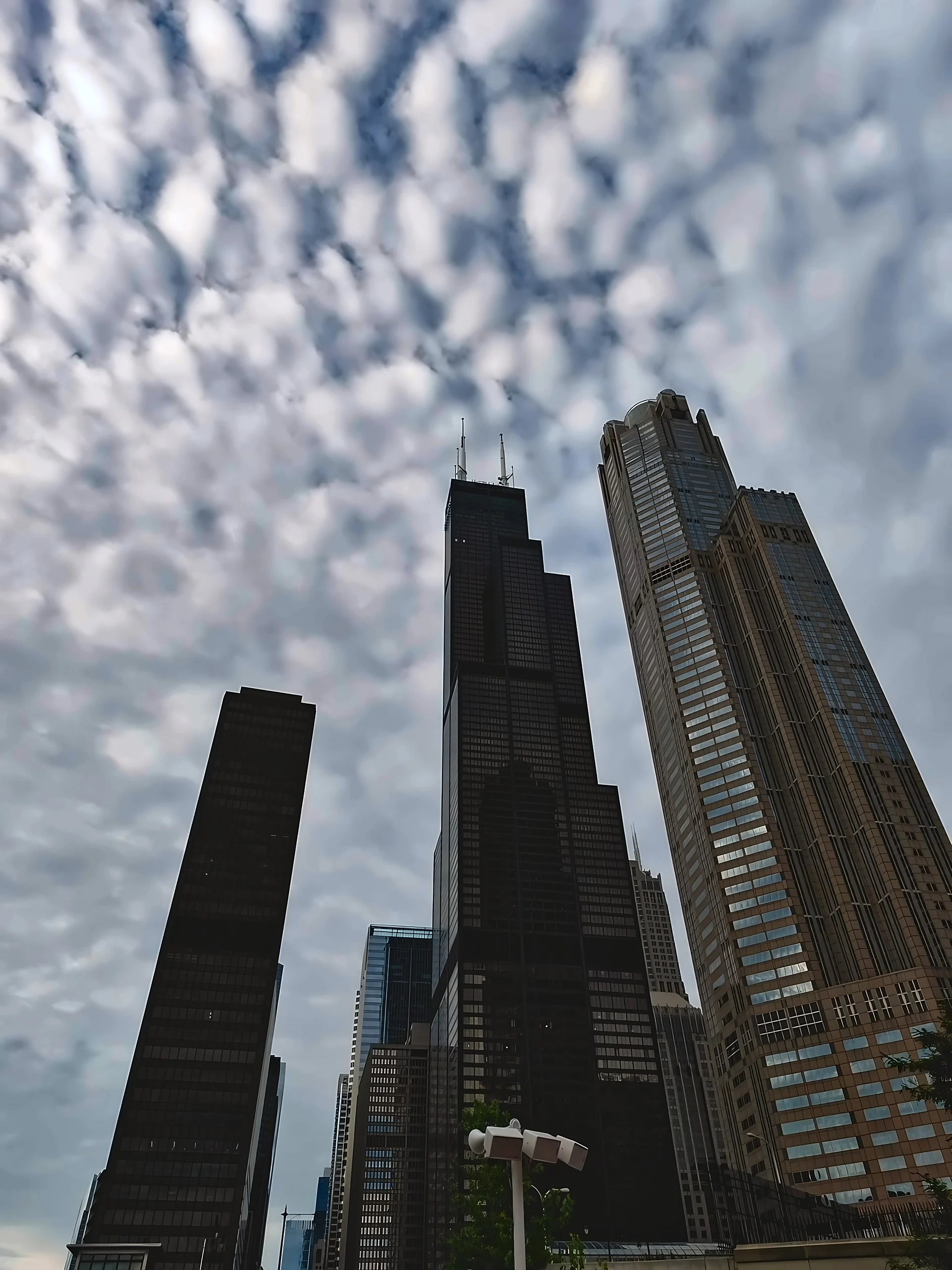 Willis Tower's twin antennas and stepped black facade rise beside a pale skyscraper beneath rippled clouds.