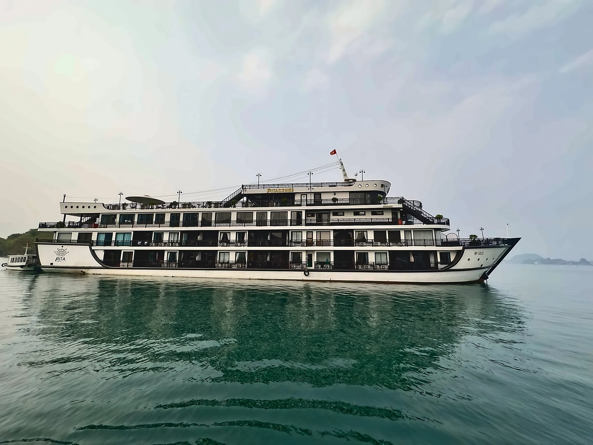 The full white RITA cruise ship and a small tender sit above rippling reflections and curved wave patterns in the bay.