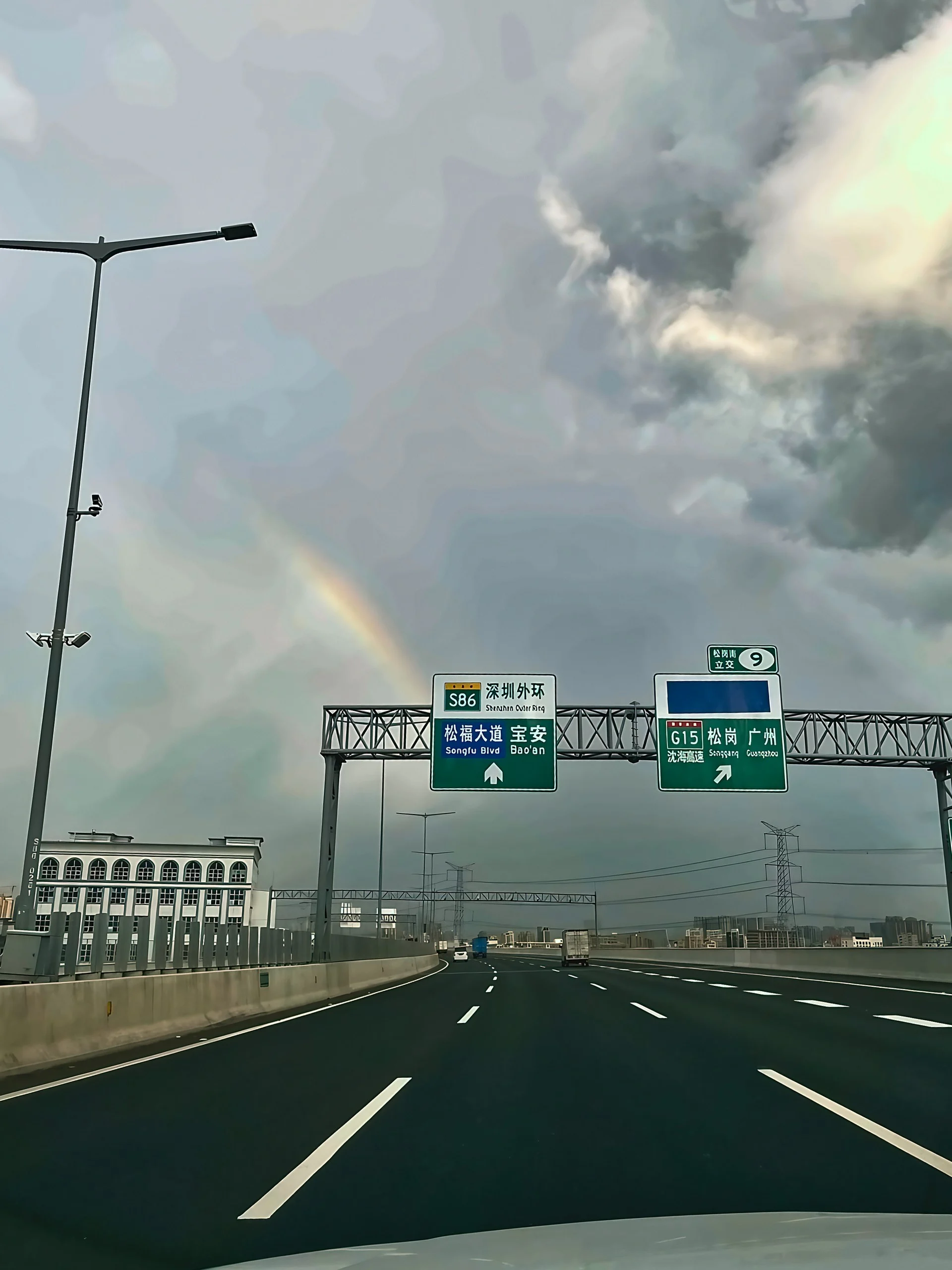 A rainbow appears above Shenzhen Outer Ring and G15 direction signs beneath a sky filled with contrasting clouds.
