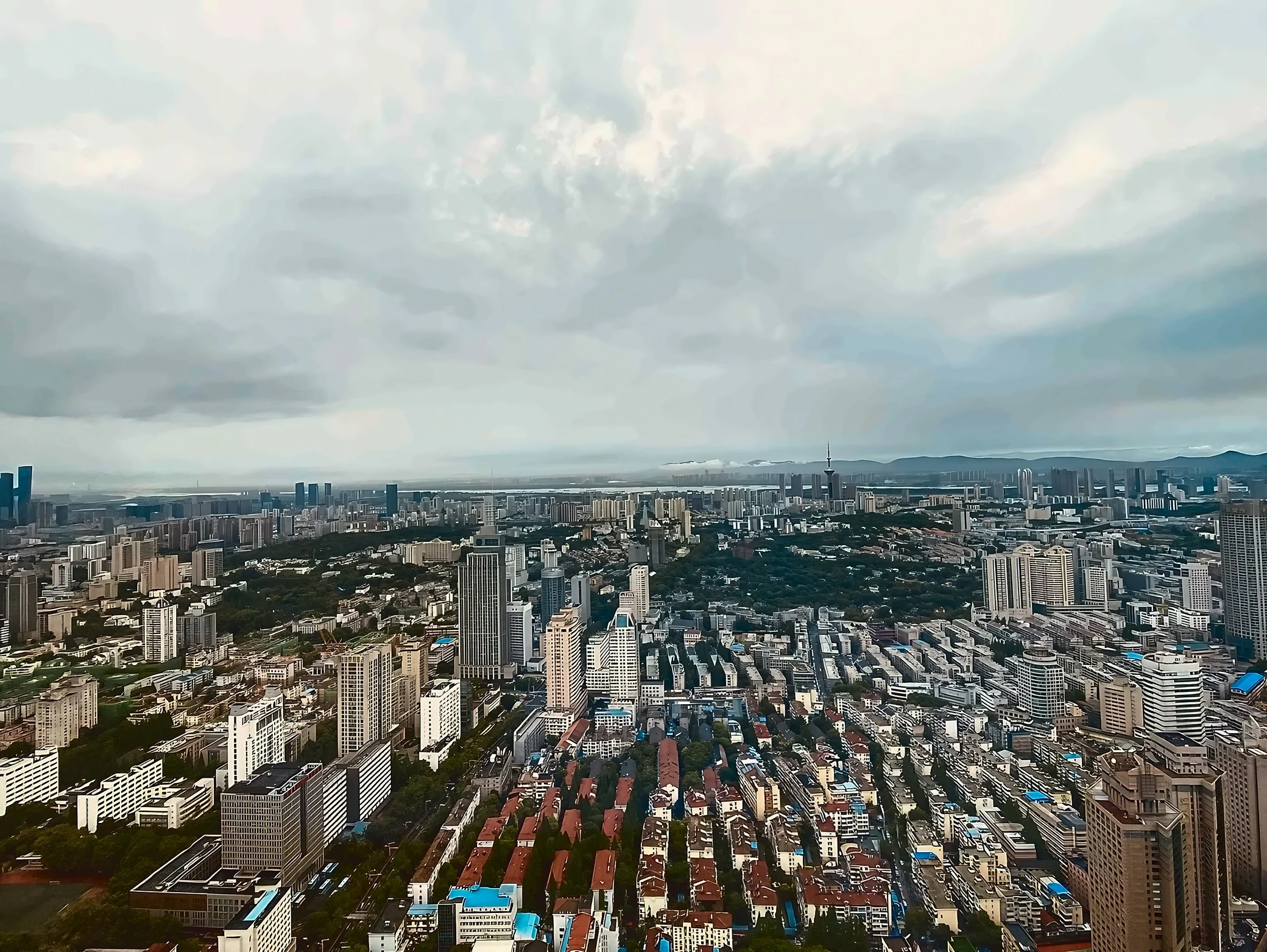 Rows of red-roofed homes, trees, and high-rise buildings fill a panoramic view of Nanjing, with a television tower and low hills in the distance.