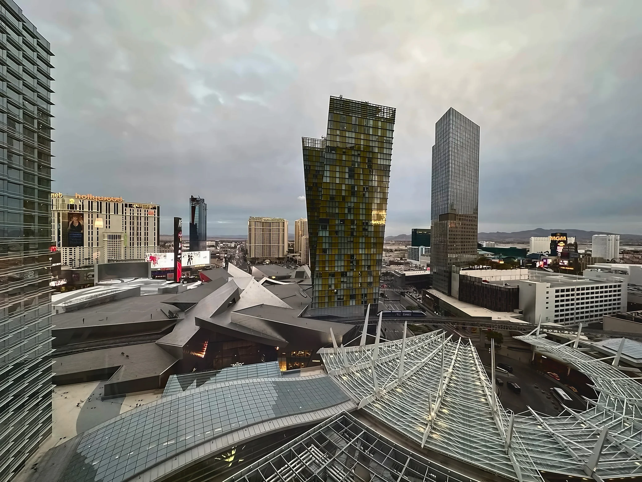 A broad CityCenter view features Veer Towers, angular shopping-center roofs, elevated tracks, and white lattice canopies beneath an overcast sky.