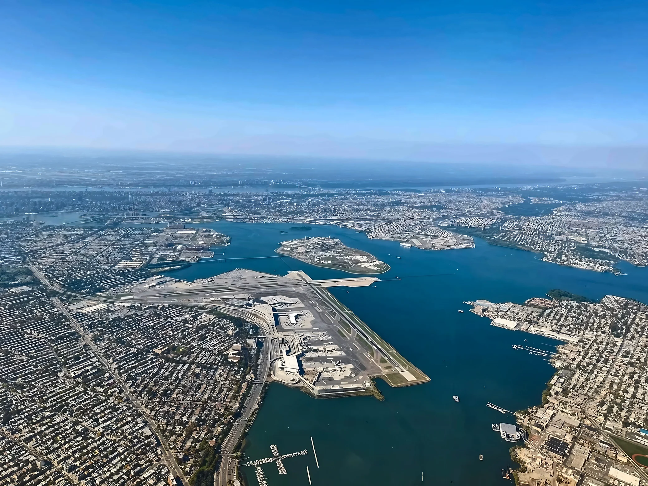 LaGuardia Airport's intersecting runways, terminals and parked aircraft sit beside broad waterways, an island and dense New York neighborhoods.