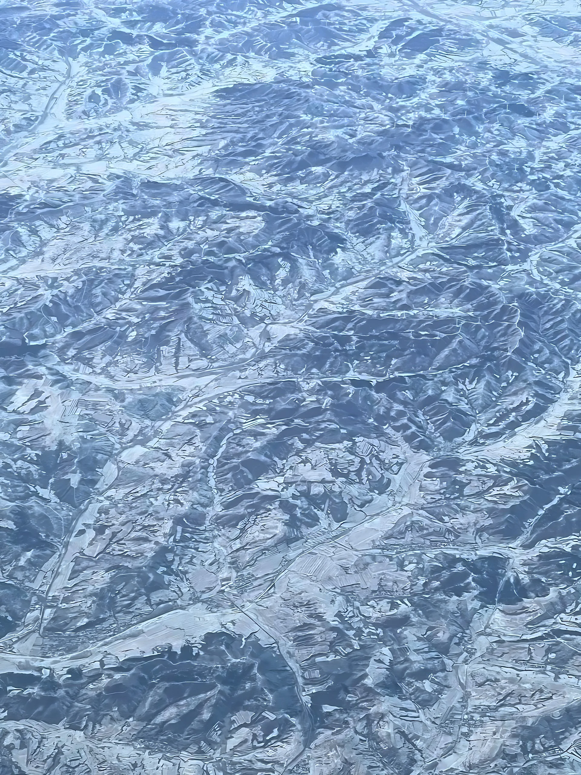 An aerial view shows snow-lined hills, branching valleys, patchwork fields and roads forming intricate patterns across the terrain.