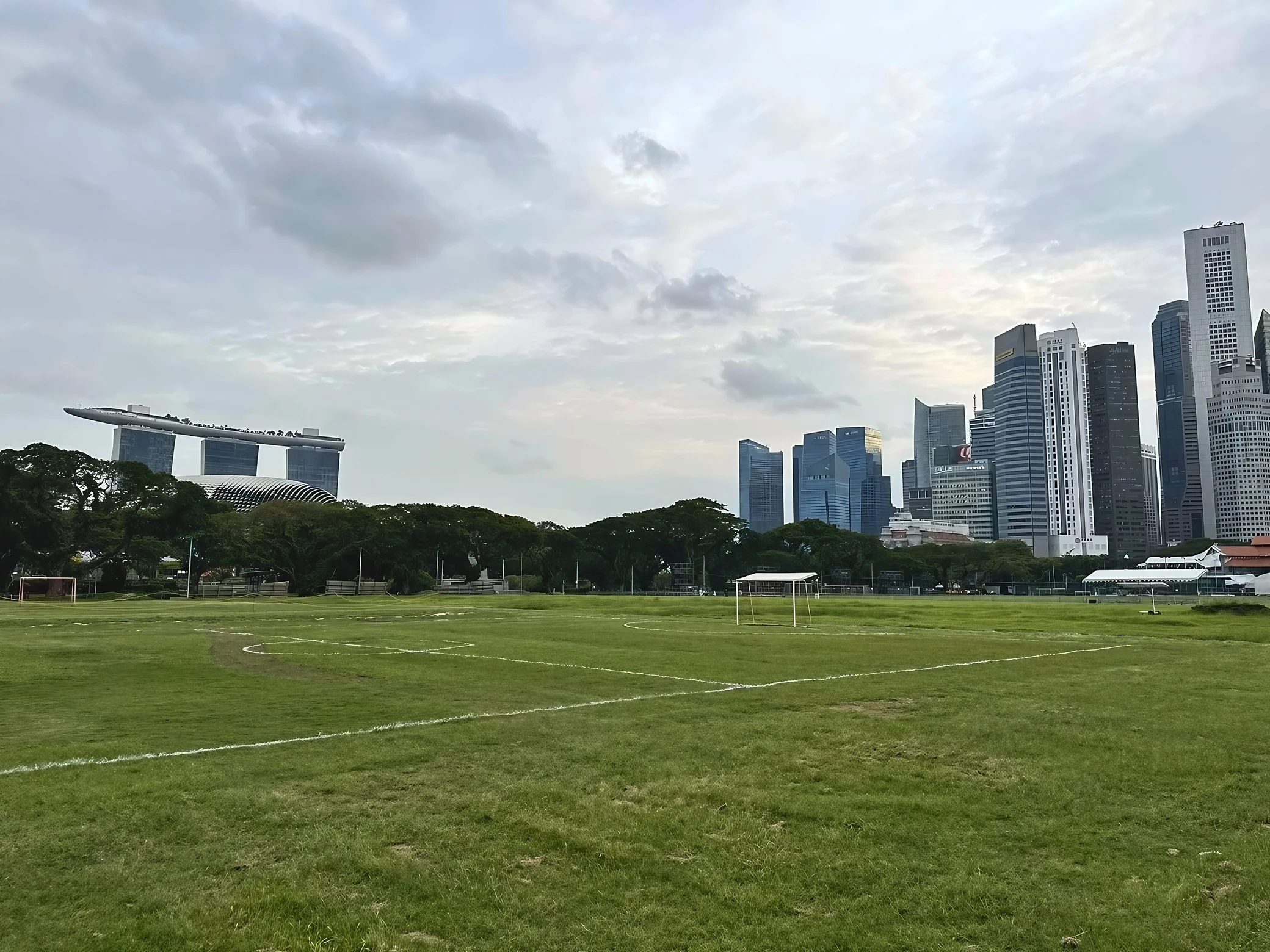 The Padang's white field markings and football goals sit between Marina Bay Sands on the left and Singapore's downtown towers on the right.