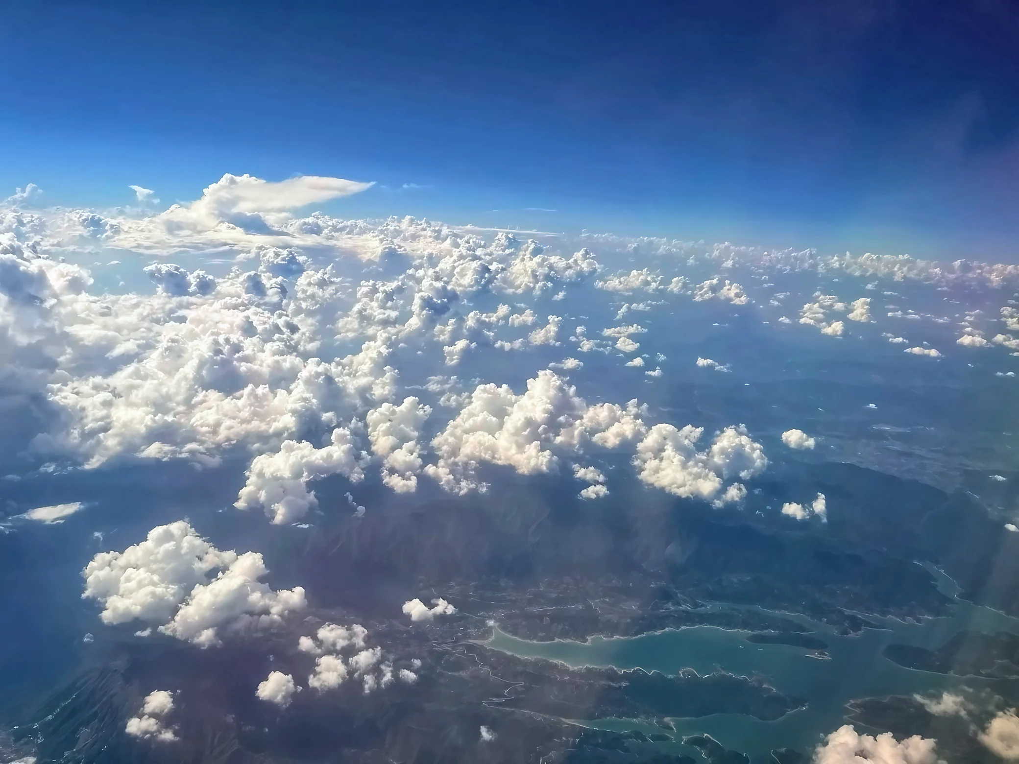 Scattered white clouds stretch above mountain ridges and a branching blue-green reservoir, with faint roads along the shore.