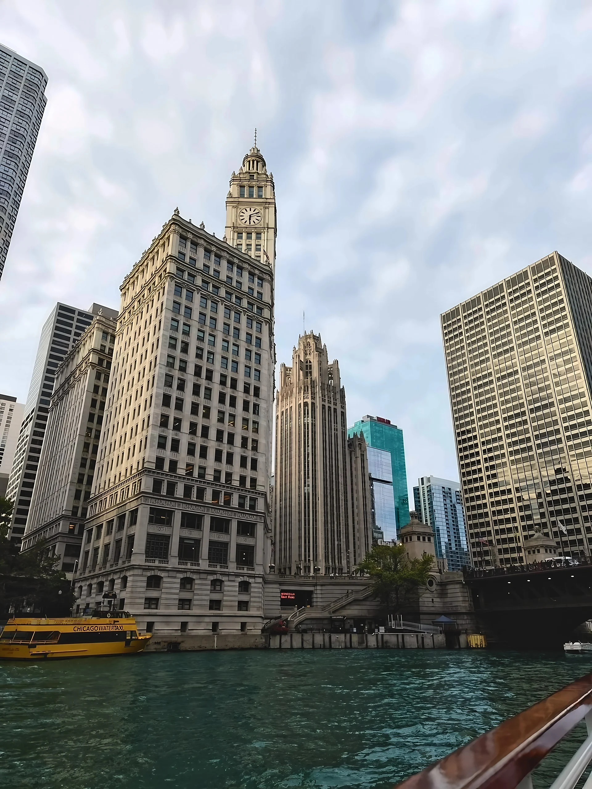 A yellow Chicago Water Taxi appears below the Wrigley Building and Tribune Tower, with the DuSable Bridge to the right.