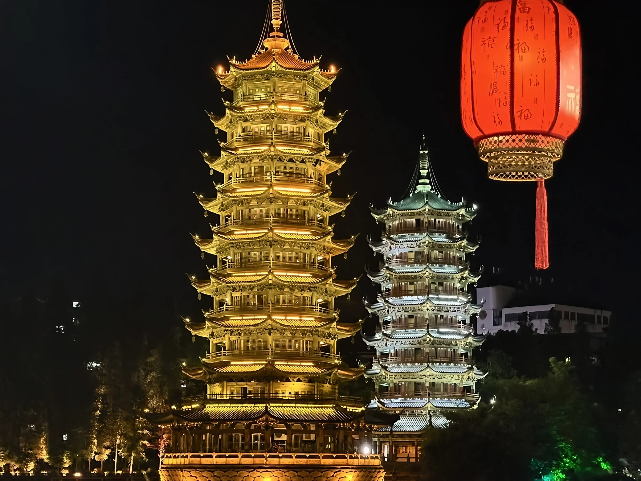 The illuminated golden Sun Pagoda and silver Moon Pagoda stand beneath a red lantern decorated with Chinese blessings.